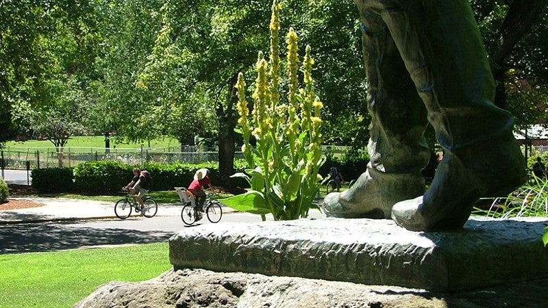 Feet of the Pioneer Father statue with people on bikes on campus