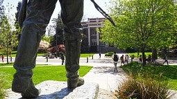 Feet of the Pioneer Father statue with people on campus